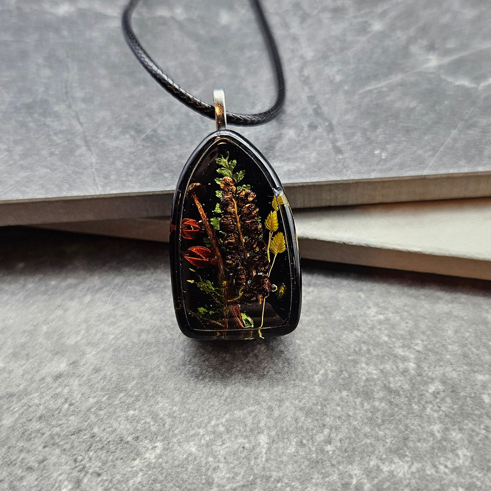A pendant with real mushrooms and ferns set in resin on a black background