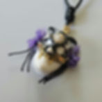 A mixed-media pendant of a black cat skull mask with gem & flower embellishments, placed on a blank white face