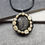Thumbnail: A ring of teeth surrounding a flashy yellow labradorite, on a black cord.