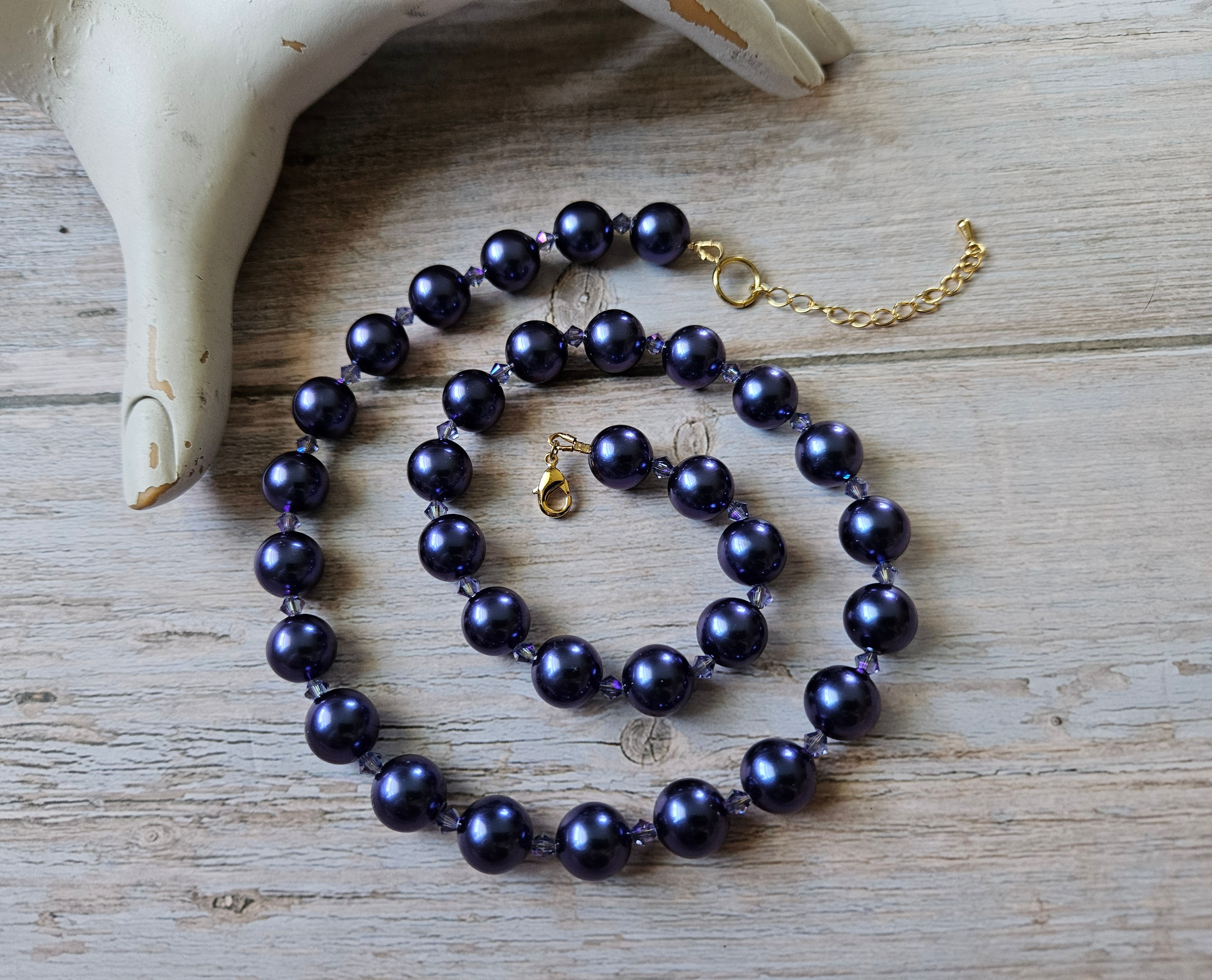 A purple pearl necklace with lavender crystal accents beads and a gold toned clasp.