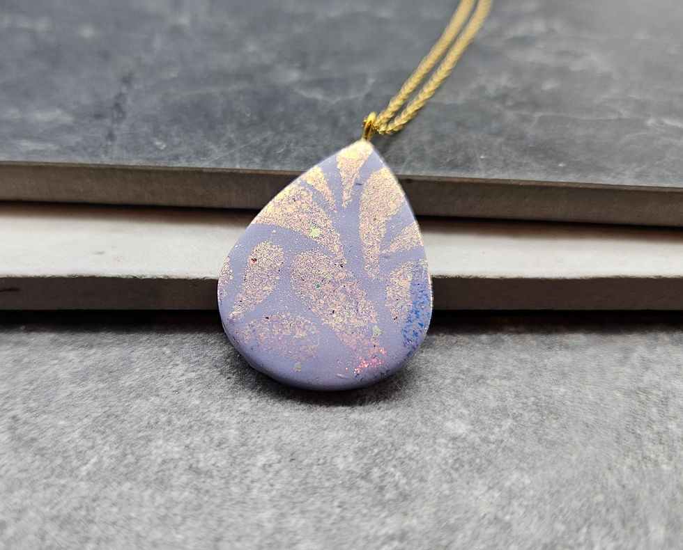 A large lavender teardrop with golden pigment applied via a stencil onto it.