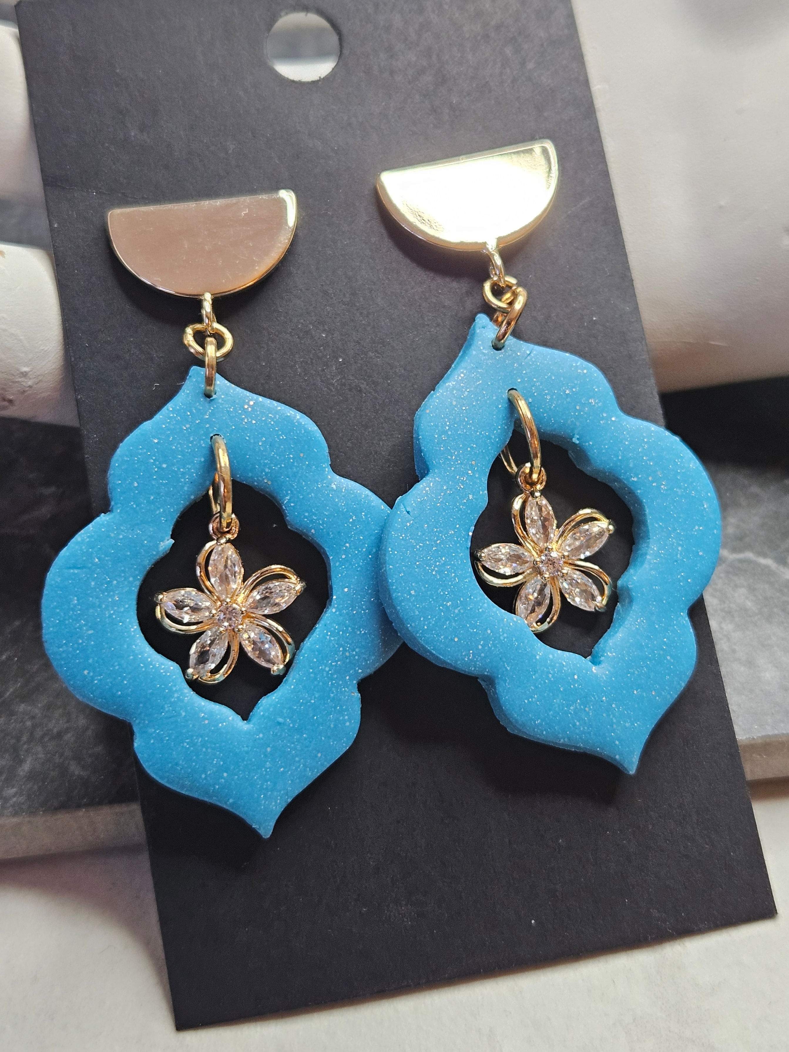 Earrings with sky blue Moroccan windows with a cz flower charm inside, beneath gold toned half moon discs.