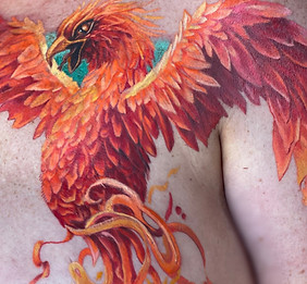 Intricate tattoo of an orange and red phoenix tattooed on a chest onto a breast with a mastectomy scar