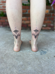 symmetrical floral tattoo on back of ankles; black and grey floral tattoo