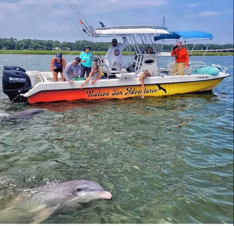 A group of people on a boat looking a dolphin in the water