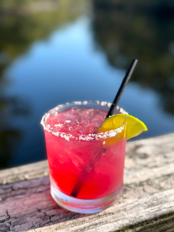 close up of a pomegranate margarita with salt lim and lime on the railing overlooking water