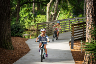 two young girls riding down a path off the bridge wearing helmets and smiling