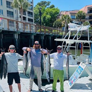 3 men holding a bunch of fish with boat and buildings in the background