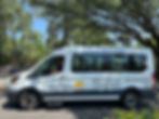 White shuttle van labeled "Dunes Buggy" on a sunny day. Driver inside. "FREE In-Resort Transportation" text visible. Trees and bikes in the background.