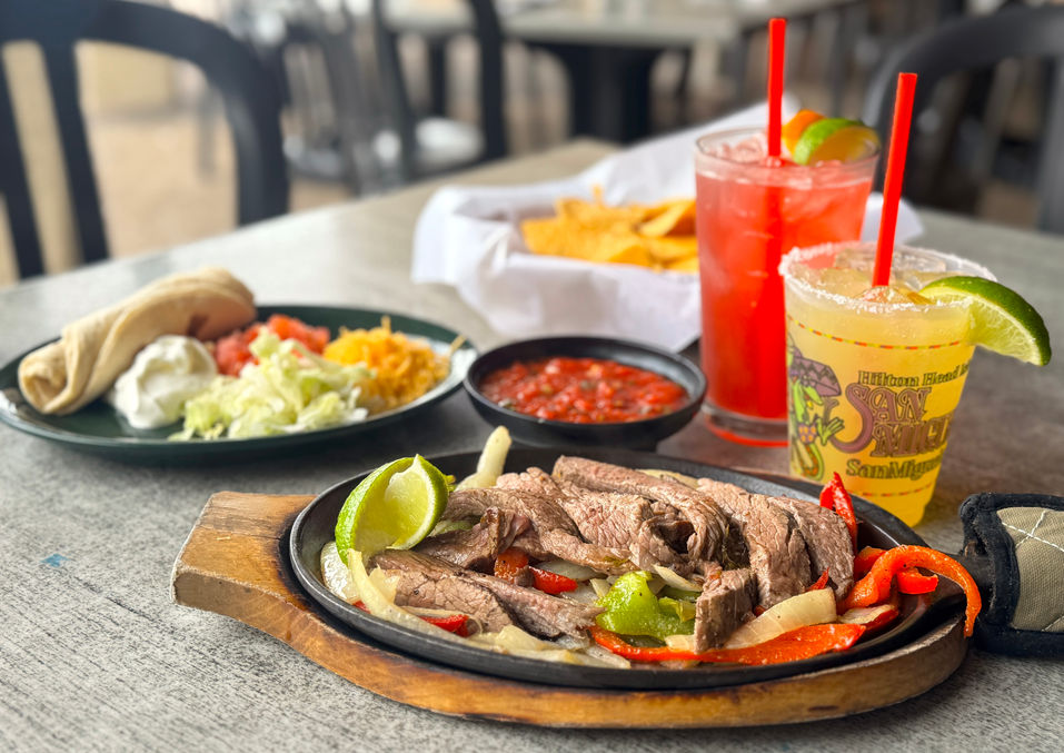 closeup of steak fajitas and all of the sides next to two margartias