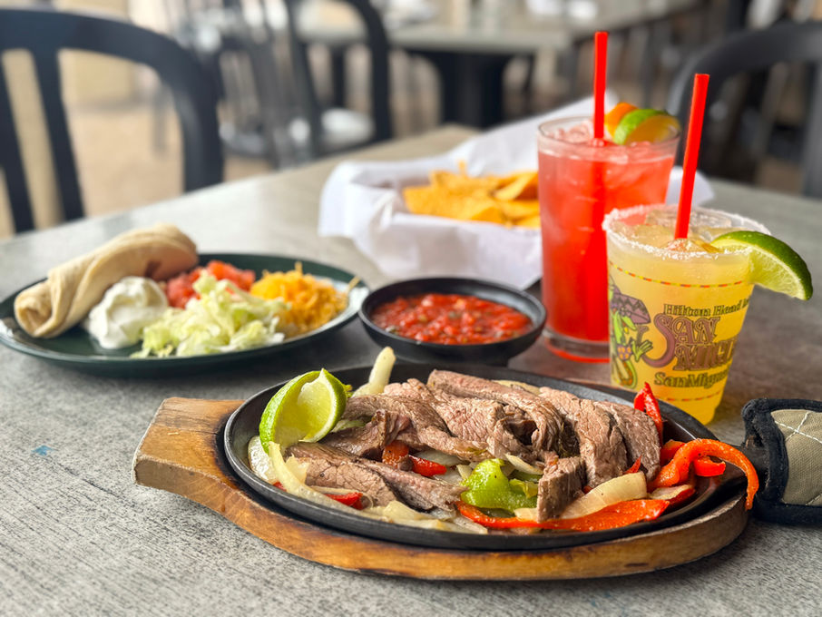 closeup of steak fajitas and all of the sides next to two margartias