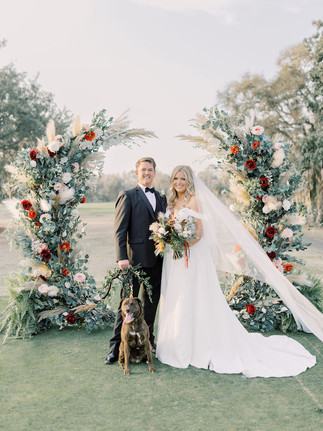 bride and groom with their dog posing under the floral wedding Arbor