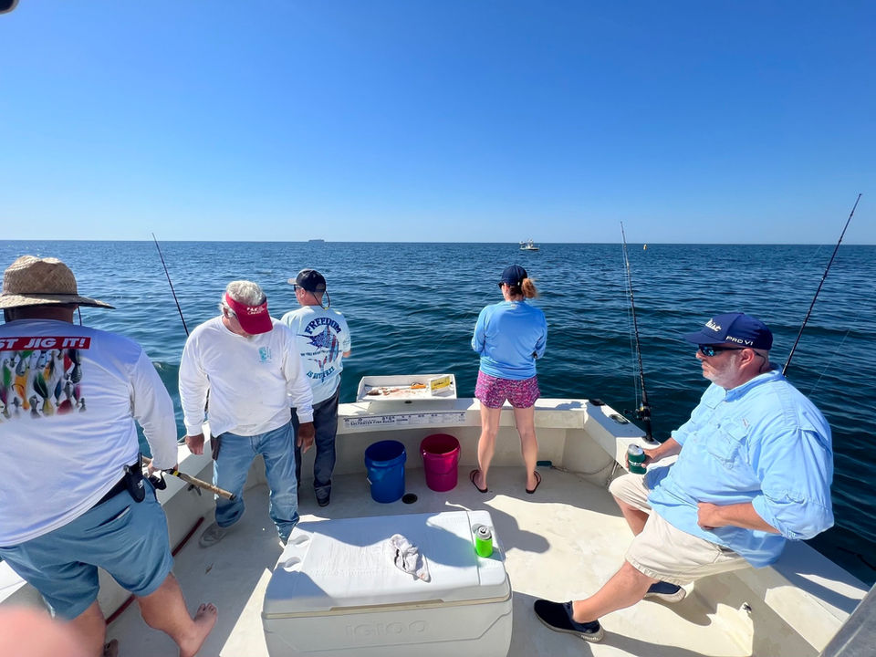 group of people in the stern of the fishing boat overlooking the water while fishing