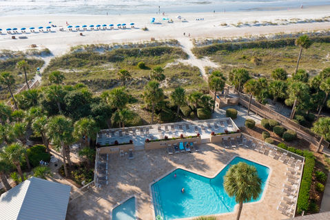 aerial view of a large oceanfront pool as well as a pathway to the beach lined with blue umbrellas