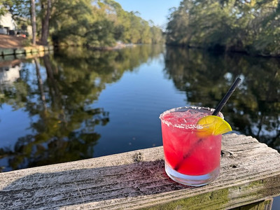 close up of a pomegranate margarita with salt lim and lime on the railing overlooking the lagoon