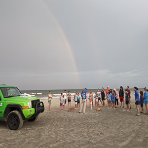 green jeep and students learning at a Turtle Talk on the beach with a rainbow in the sky
