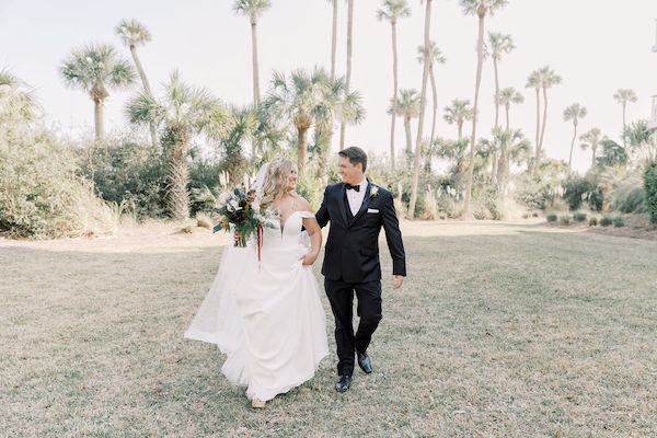 bride and groom walking looking at each other with tree line in the back
