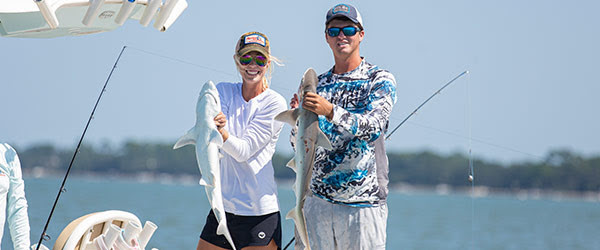 man and woman holding small sharks on fishing boat