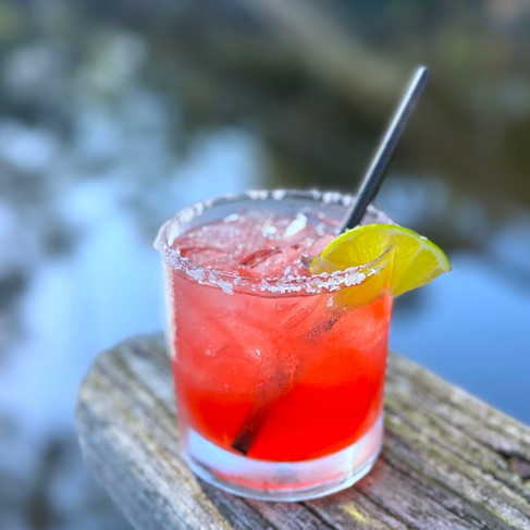 close up of a pomegranate margarita with salt lim and lime on the railing with water in the background
