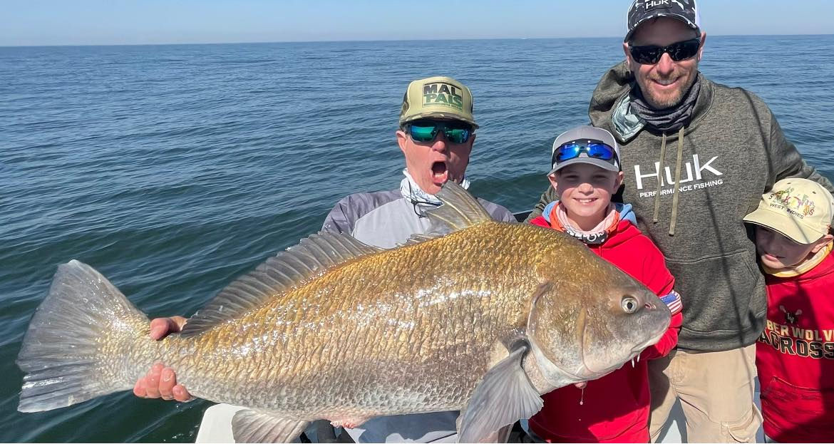 Man shows his large fish off while two kids and man pose next to him.