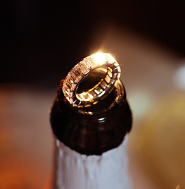 A sparkling diamond ring perched on the neck of a champagne bottle, glowing warmly in soft, ambient light.