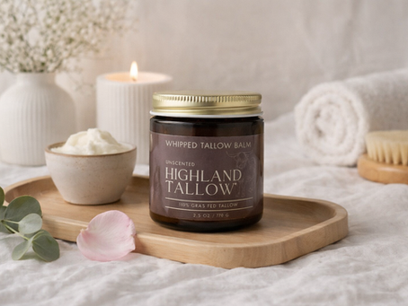 Jar of Highland Tallow Co. Whipped Tallow Balm on a wooden tray with a small bowl of tallow surounded by bath/spa items such as a candle and towel