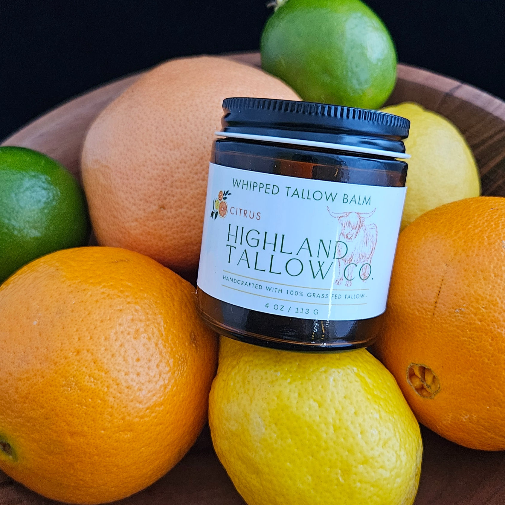 A 4 oz amber glass jar with a label that reads Highland Tallow Co. Citrus Whipped Tallow Balm sitting in a bowl with fruit
