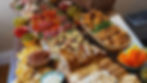 A colourful grazing of snacks on a wooden table includes crackers, dips, meats, cheese, pastries, and fruits, creating a festive atmosphere.