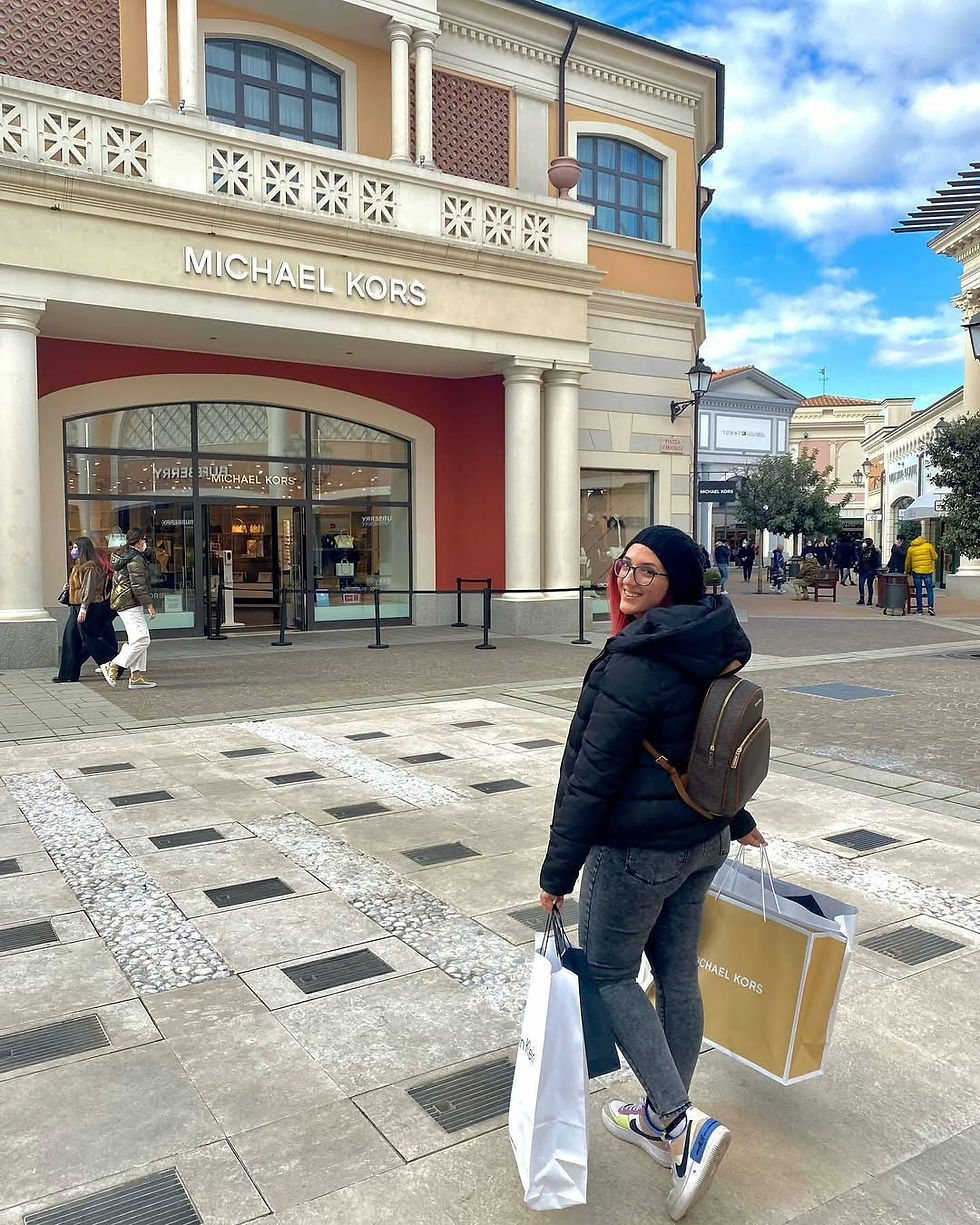 A woman smiles while holding multiple shopping bags outside the Michael Kors store at Castel Romano Designer Outlet, capturing the thrill of outlet shopping in Rome.