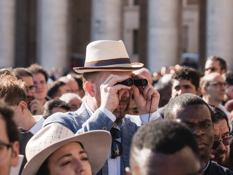 Crowd of tourists in St Peter’s Square, Vatican City; a man in a Panama hat peers through binoculars during a Papal audience. Photo: giannicipriano.