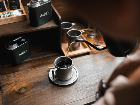 a person pouring hot water from a kettle into a Vietnamese coffee-making kit on wooden table