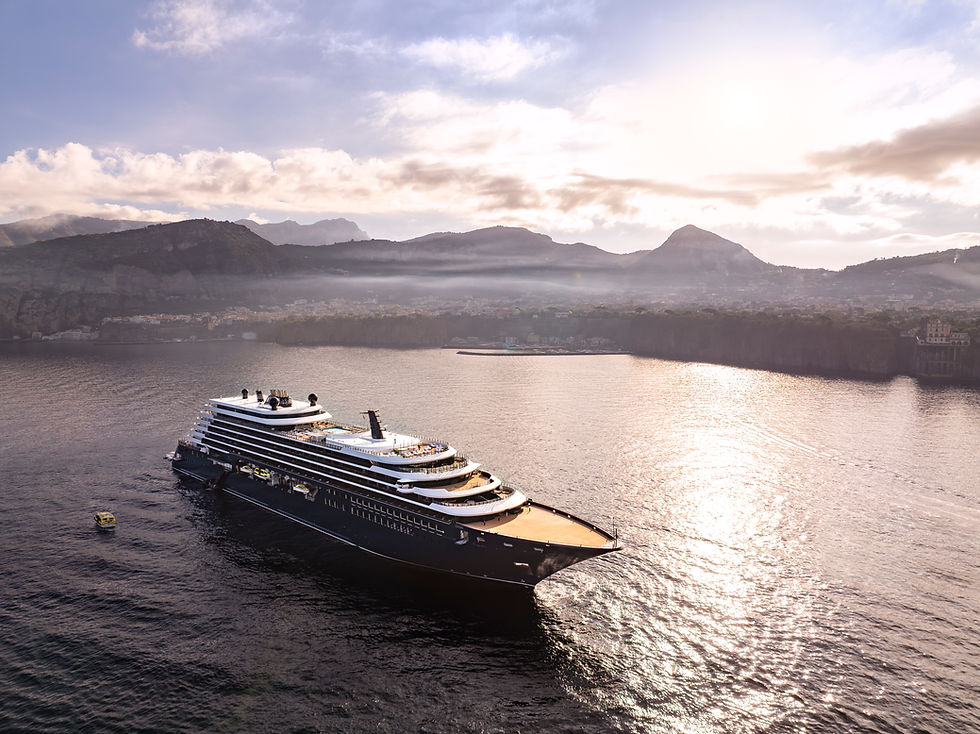Cruise ship sailing on calm waters beneath a cloudy sky with distant mountains. Sunlight reflects on the sea, creating a serene atmosphere.