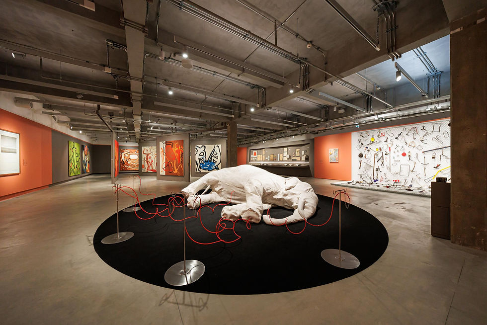 Modern art gallery with a white animal sculpture on a black oval platform, red cables, and colorful abstract paintings on the walls