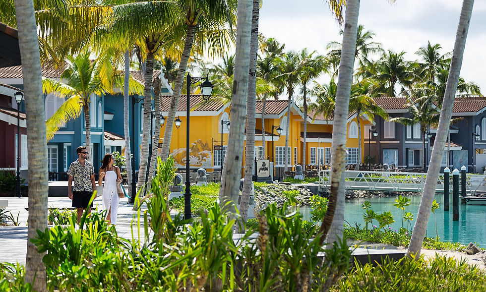 Couple strolling by a turquoise lagoon in a tropical resort with palm trees and colorful villas under bright sun