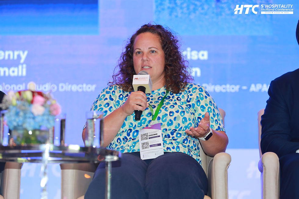 Woman speaking into a microphone at HTC Hospitality Thailand Conference panel, with a blue stage backdrop and logo visible.