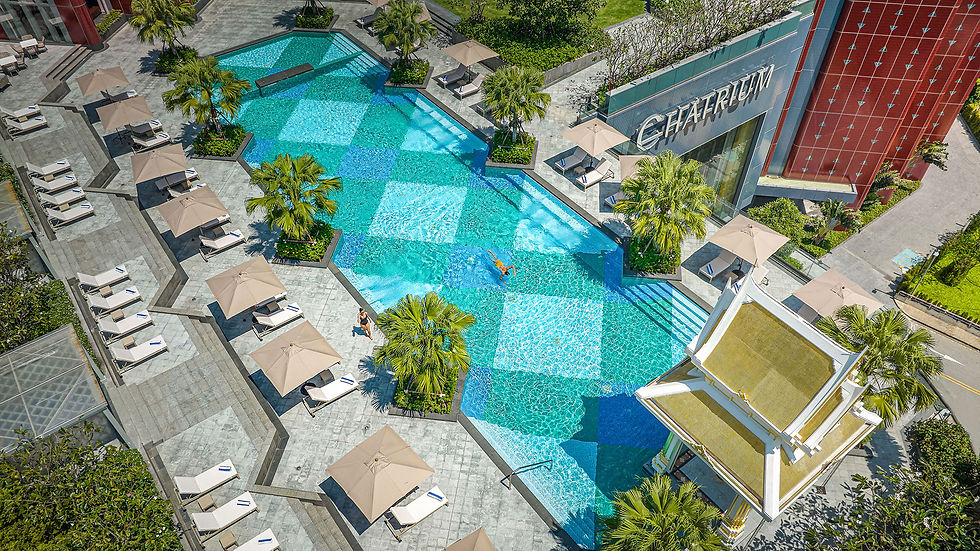 Aerial view of Chatrium luxury resort pool with a swimmer, beige umbrellas, loungers, palm trees, and turquoise water.