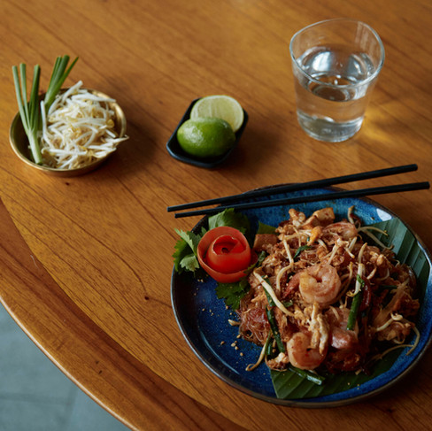 a plate on pad tha with a glass of plain water, lime wedges, bean sprouts and chive on a wooden table