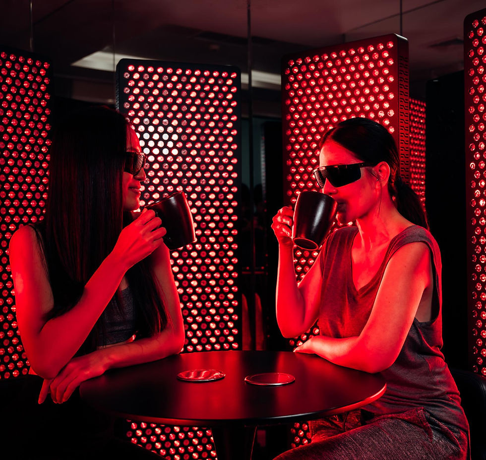 Two women in sunglasses sip black mugs at a table in a red LED-lit room, creating a futuristic, relaxed mood.