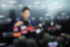 Man speaking at a press conference with many microphones, before an EVOLVE Mixed Martial Arts backdrop and cameras.