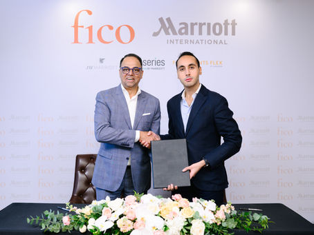 Two men in suits shake hands at a Fico and Marriott International event, with one holding a folder and floral table display.