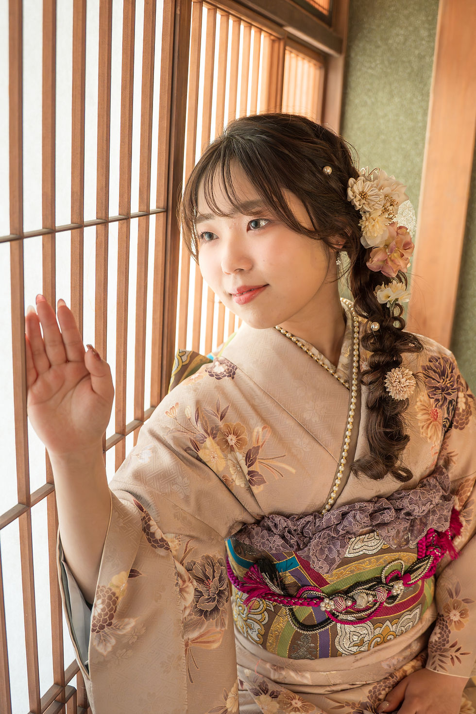 障子のそばで、花飾りを付けた着物姿の女性が窓に手を添え、やわらかな光の中で静かに微笑んでいる】【。
