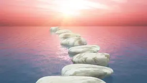 Caminho de pedras claras sobre a água em direção ao horizonte rosado ao amanhecer, simbolizando transição, recomeço, coragem emocional e novos ciclos de vida.