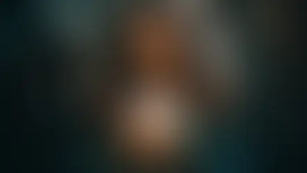Mulher sorridente segurando flor de lótus iluminada em ambiente místico com luzes suaves ao fundo.