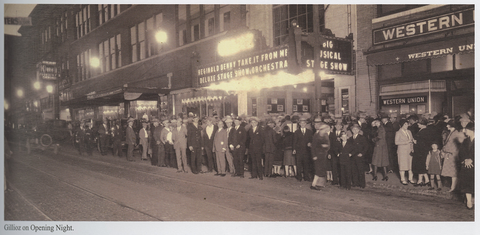 A thick crowd of people spill out into the street in front of the Gillioz, which is lit up on opening night. Men and women wear suits and hats, and the marquee advertises Reginald Denny Take It From Me.