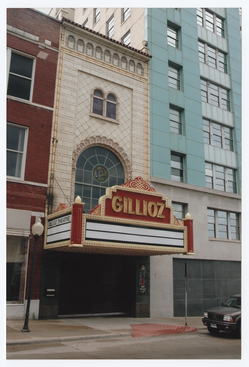 The exterior facade of the Gillioz Theater has an Art Deco style rounded window and a red decorative marquee.