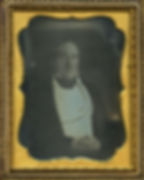 A seated man with his hands clasped. Side-to-side brushstrokes are visible across the black and white image.