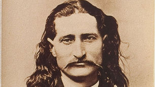 A sepia toned portrait of a man with long hair and a long mustache wearing a high collar and jacket with lapel.