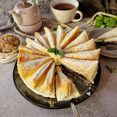 Fruchtiger Sahnekuchen in Fächerform mit Puderzucker, daneben Teekanne, Tasse und Deko auf gemütlichem Tisch.