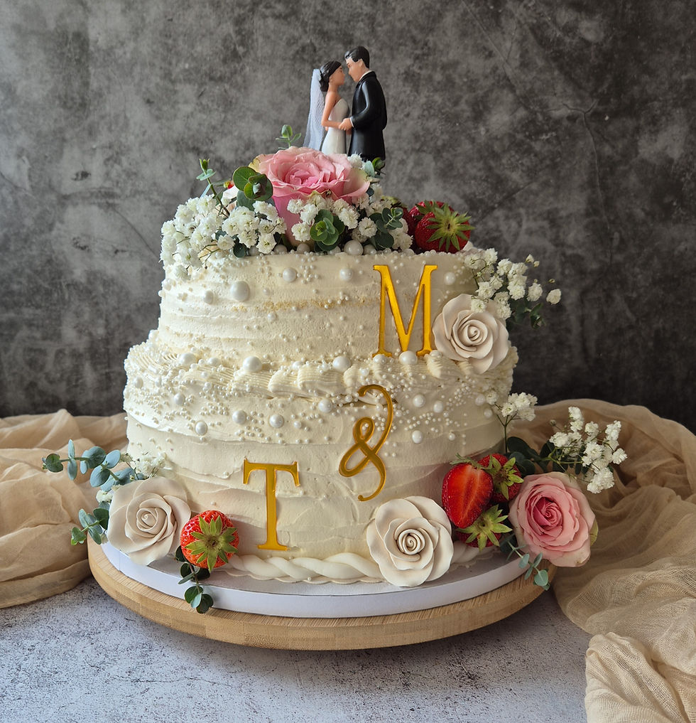 Zweistufige weiße Hochzeitstorte mit Brautpaar-Figur, Blumen, Erdbeeren und goldenen T & M vor grauem Hintergrund.