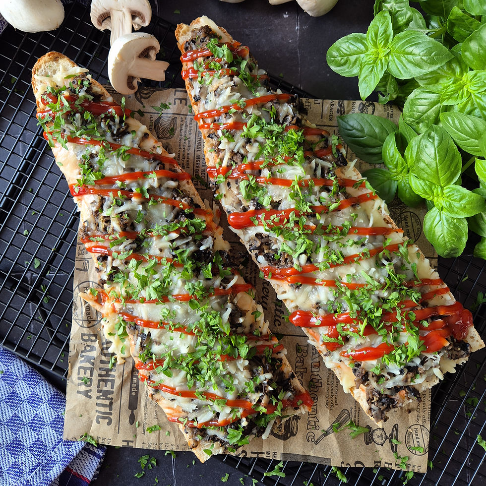 Zwei überbackene, mit Pilzen und Kräutern belegte Baguettes mit Ketchup auf Backpapier, daneben frischer Basilikum.